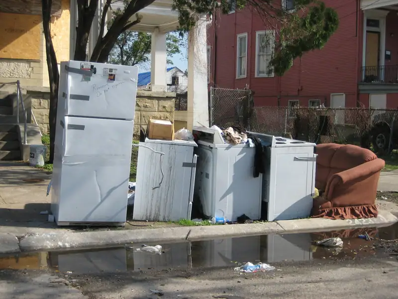 An old refrigerator, washing machines and an armchair set out at the curb for disposal