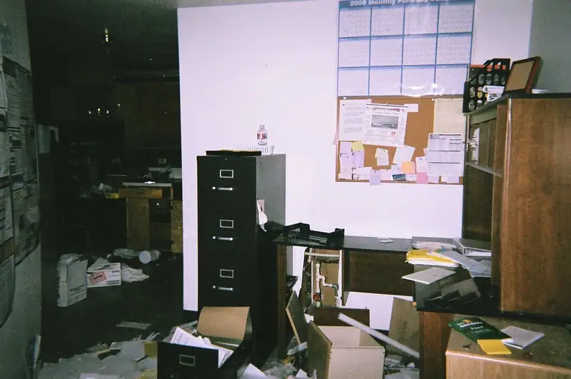 An abandoned office with filing cabinets, a desk and papers and boxes strewn across the floor