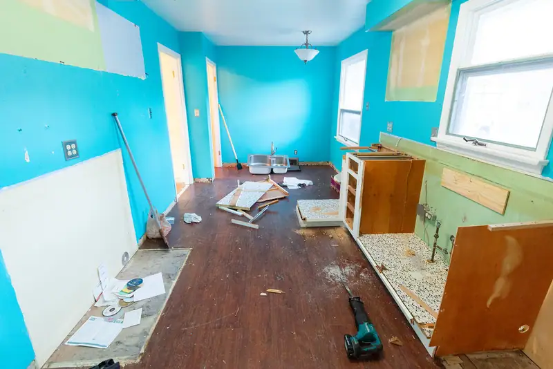 A kitchen mid-renovation with cabinets and countertops torn out and construction debris scattered across the floor