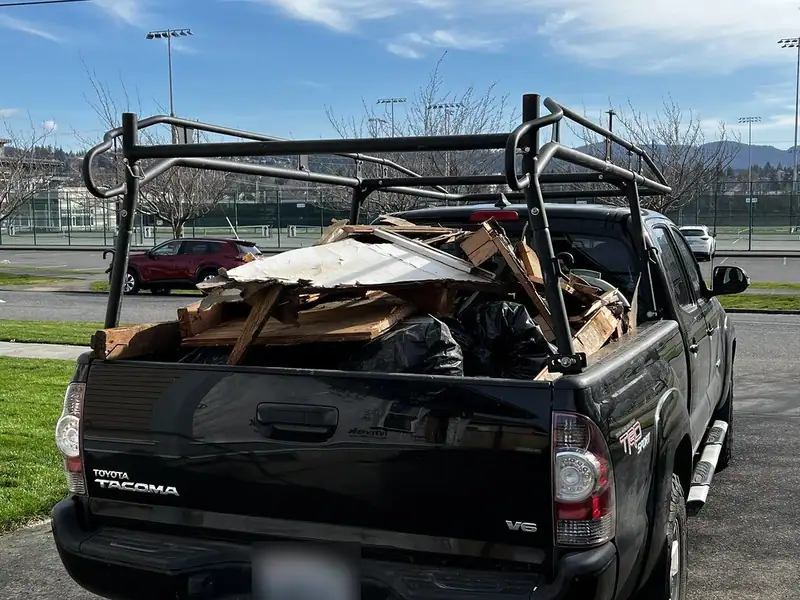 A pickup truck with a ladder rack, its bed loaded with scrap wood and bagged debris for a dump run